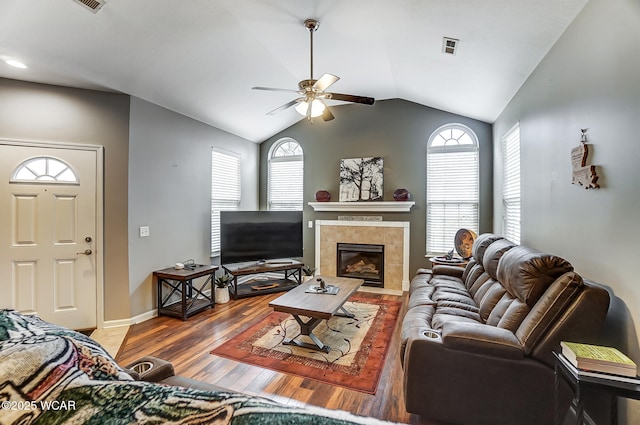 living room with a tile fireplace, wood-type flooring, vaulted ceiling, and ceiling fan