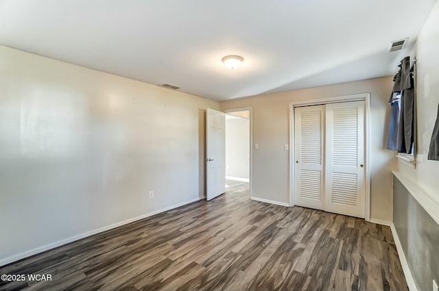 unfurnished bedroom with a closet, visible vents, baseboards, and wood finished floors