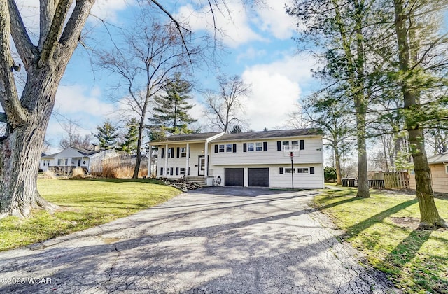 split foyer home with aphalt driveway, fence, a garage, and a front lawn
