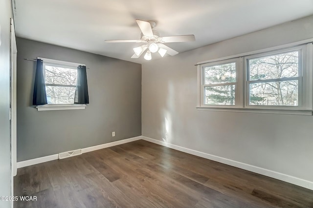 empty room with visible vents, a ceiling fan, dark wood-type flooring, and baseboards