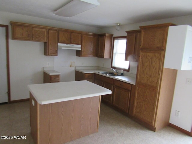 kitchen with brown cabinetry, light floors, a kitchen island, a sink, and under cabinet range hood