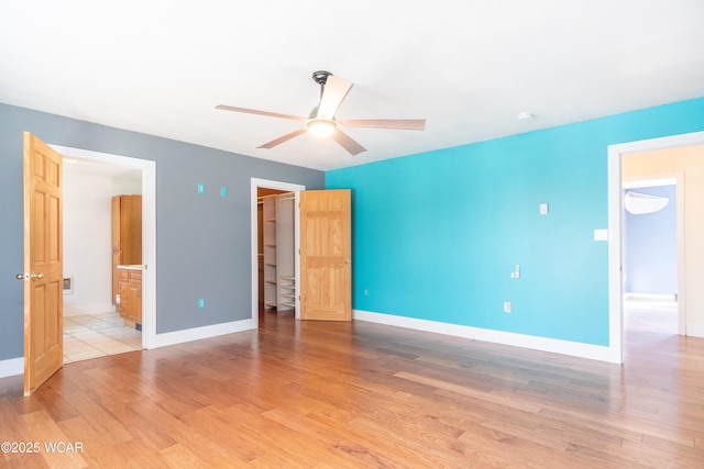 unfurnished bedroom featuring a spacious closet, light wood-type flooring, ensuite bath, ceiling fan, and baseboards