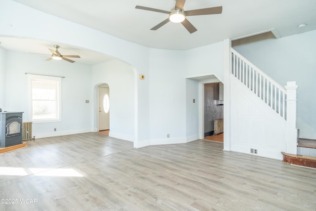 unfurnished living room featuring stairway, radiator heating unit, ceiling fan, arched walkways, and light wood-style flooring