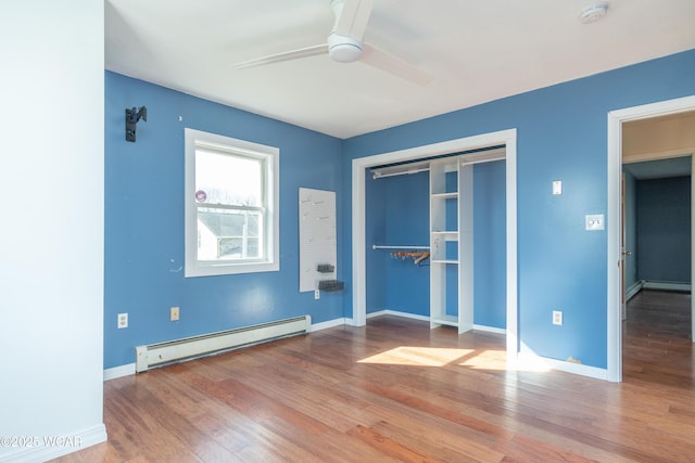 unfurnished bedroom featuring a baseboard heating unit, baseboards, wood finished floors, and a closet