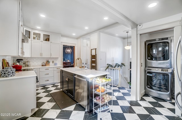 kitchen featuring sink, white cabinets, hanging light fixtures, stacked washer and clothes dryer, and a center island with sink