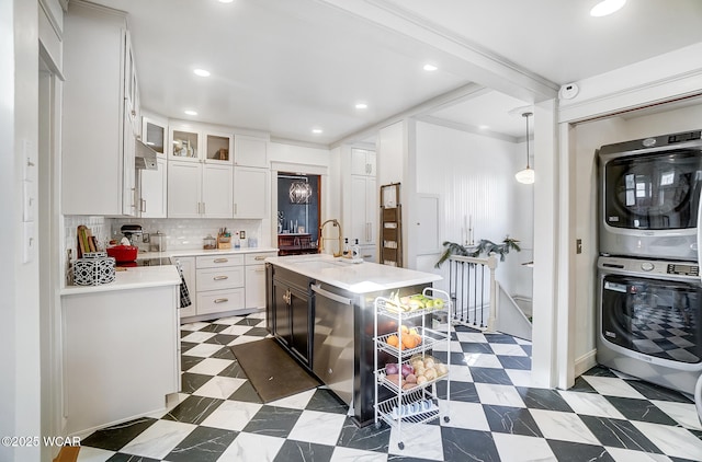 kitchen with sink, a center island with sink, pendant lighting, stacked washer / dryer, and white cabinets