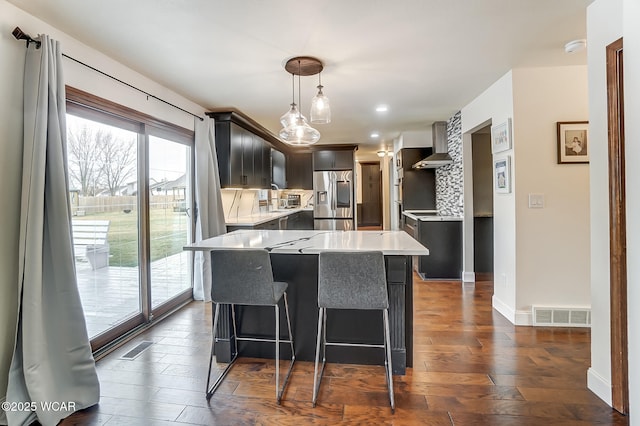 kitchen featuring a kitchen island, hanging light fixtures, stainless steel refrigerator with ice dispenser, dark wood-type flooring, and wall chimney exhaust hood