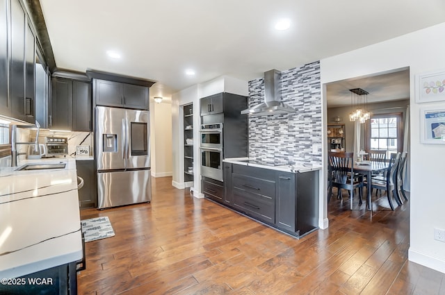 kitchen featuring appliances with stainless steel finishes, wall chimney range hood, dark hardwood / wood-style flooring, and decorative light fixtures