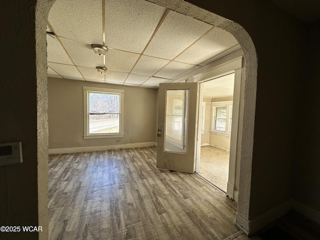 unfurnished room with wood finished floors, a paneled ceiling, arched walkways, and baseboards