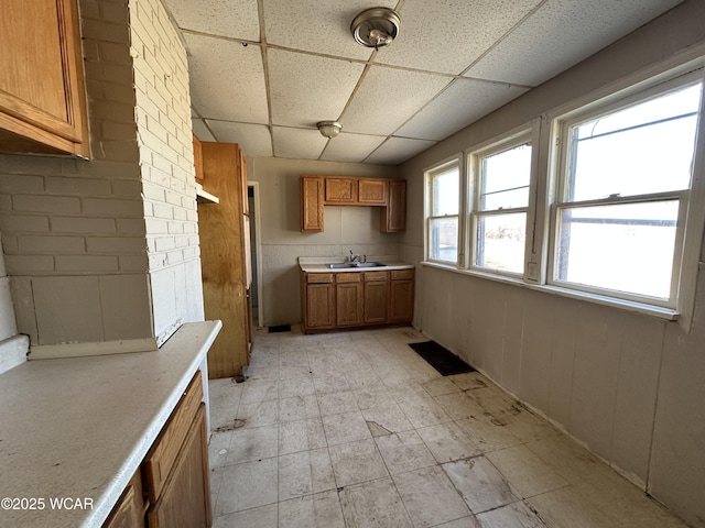 kitchen with visible vents, light countertops, brown cabinetry, a paneled ceiling, and a sink