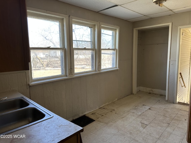 interior space with a sink, a paneled ceiling, light floors, and wood walls