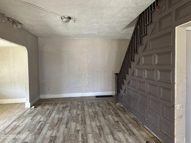 unfurnished living room with stairs, wood finished floors, baseboards, and a textured ceiling