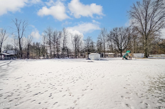 yard layered in snow with a storage shed and a playground