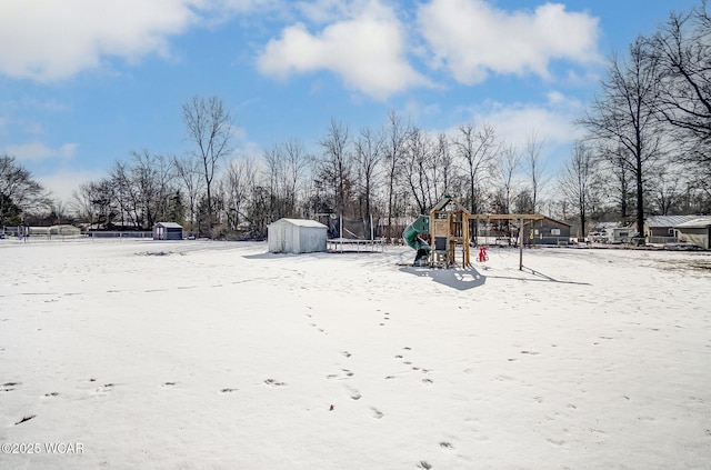 snowy yard featuring a playground and a storage unit