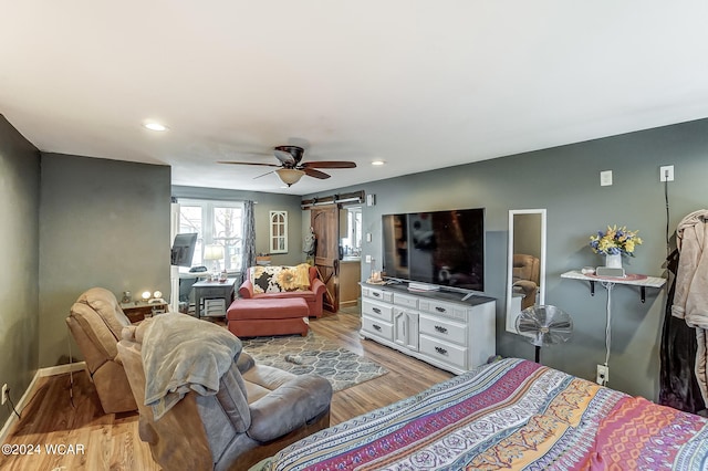 bedroom with light wood-type flooring, ceiling fan, and a barn door