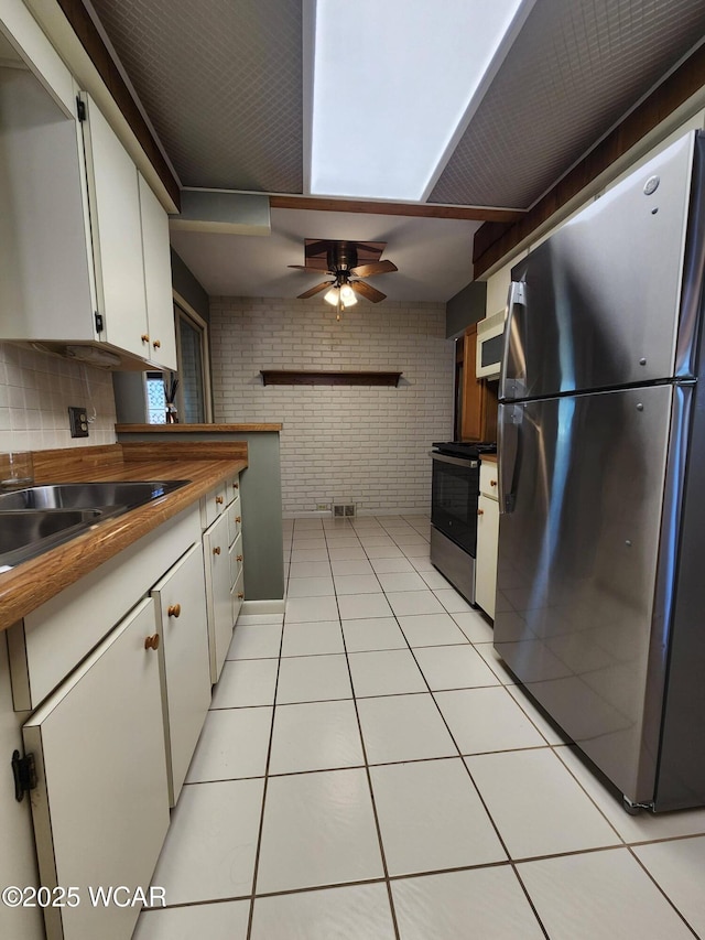 kitchen with stainless steel appliances, brick wall, light tile patterned floors, ceiling fan, and white cabinetry