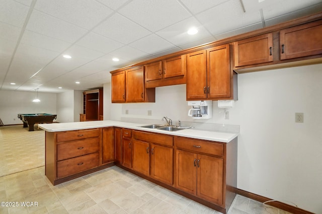 kitchen with a sink, a peninsula, brown cabinets, recessed lighting, and light countertops