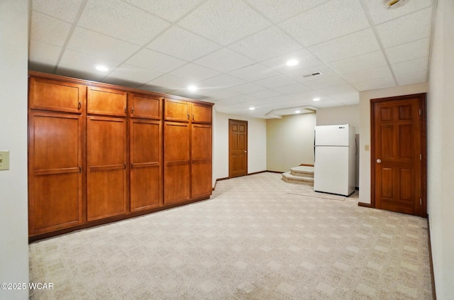 finished basement with freestanding refrigerator, a drop ceiling, stairway, and baseboards