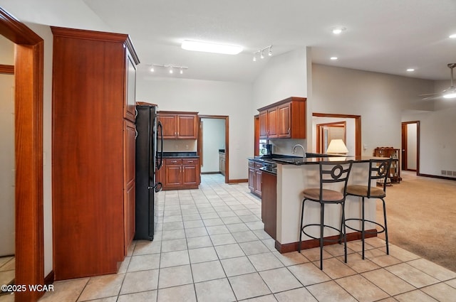 kitchen featuring freestanding refrigerator, dark countertops, a peninsula, and a kitchen breakfast bar