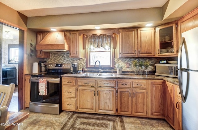 kitchen featuring stainless steel appliances, dark countertops, custom range hood, decorative backsplash, and a sink