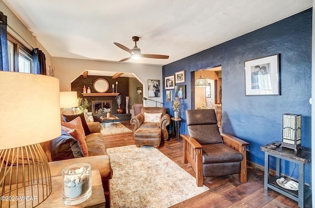 living area featuring ceiling fan, a fireplace, baseboards, and wood finished floors