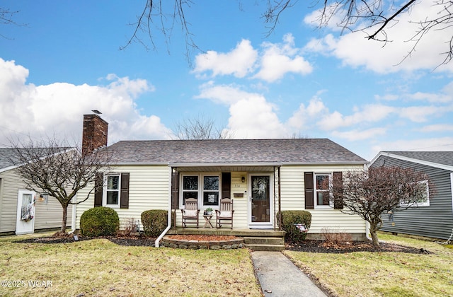 single story home featuring a shingled roof, a front yard, covered porch, and a chimney