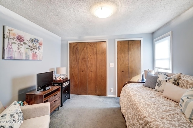 bedroom featuring a textured ceiling, two closets, and light colored carpet