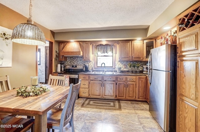 kitchen with dark countertops, custom range hood, decorative backsplash, appliances with stainless steel finishes, and a sink