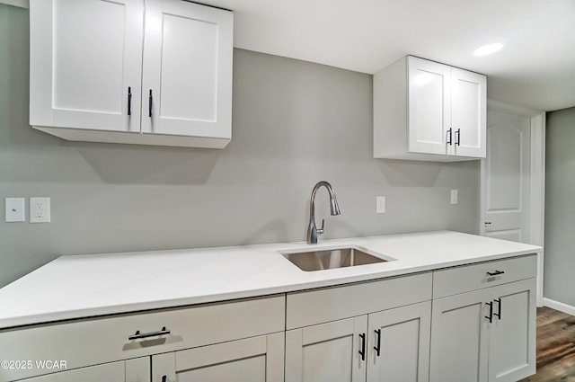 kitchen with white cabinets, light countertops, a sink, and wood finished floors