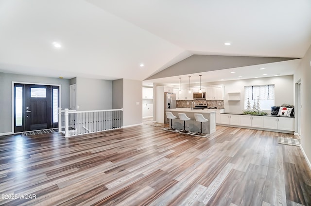 unfurnished living room with light wood finished floors, recessed lighting, a sink, vaulted ceiling, and baseboards