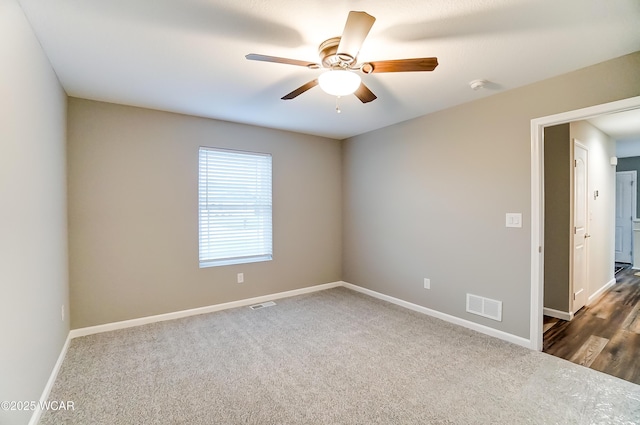 spare room with a ceiling fan, visible vents, dark carpet, and baseboards