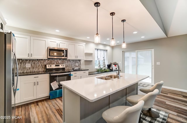 kitchen featuring decorative light fixtures, stainless steel appliances, dark countertops, white cabinets, and a sink