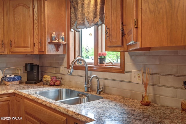 kitchen with brown cabinetry, light stone countertops, tasteful backsplash, and a sink