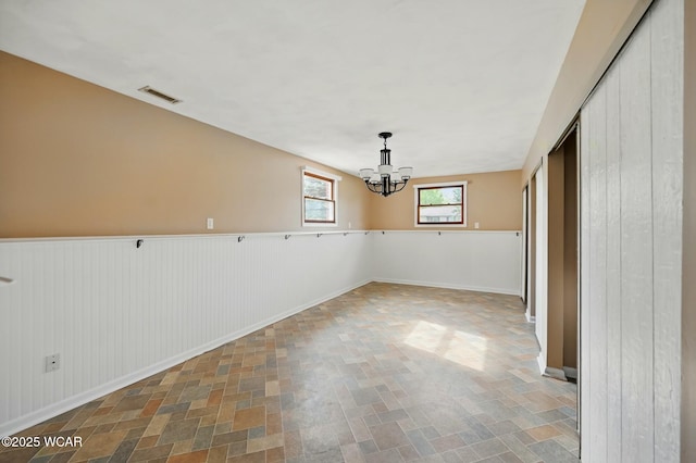 unfurnished dining area featuring baseboards, visible vents, an inviting chandelier, and a wainscoted wall