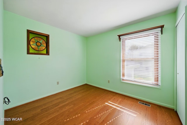 empty room with baseboards, wood finished floors, and visible vents