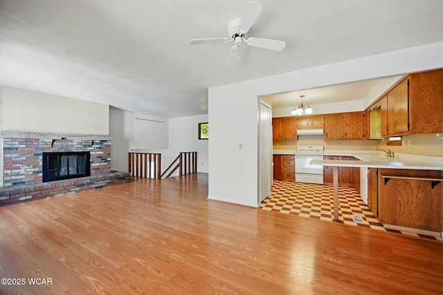 unfurnished living room with a sink, a fireplace, ceiling fan with notable chandelier, and light wood-type flooring