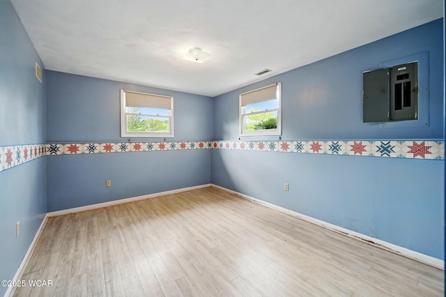 empty room featuring visible vents, plenty of natural light, wood finished floors, and electric panel