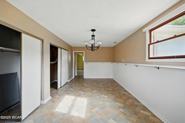 unfurnished dining area with baseboards, stone finish flooring, and a chandelier
