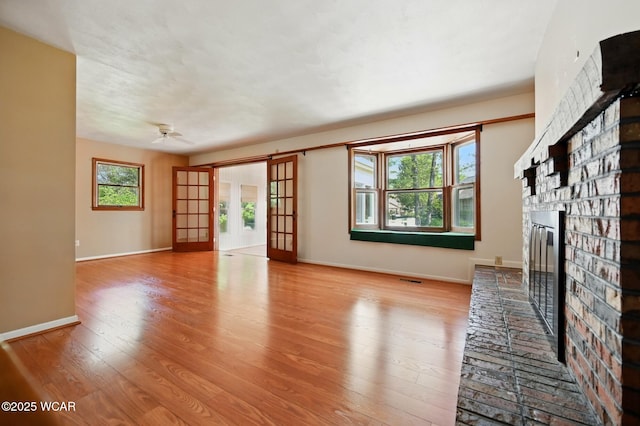 unfurnished living room with a brick fireplace, wood finished floors, baseboards, french doors, and a ceiling fan