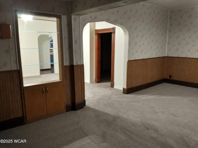 unfurnished room featuring light carpet, wainscoting, arched walkways, and wallpapered walls