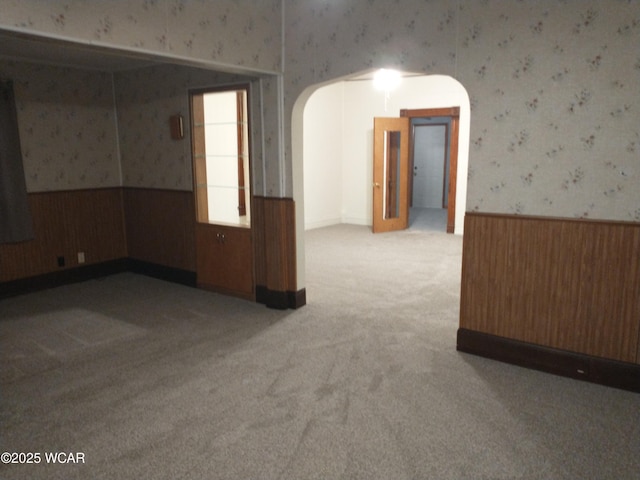 carpeted empty room with wallpapered walls, arched walkways, and a wainscoted wall