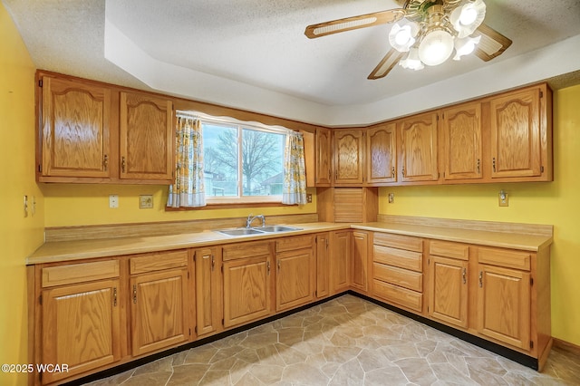 kitchen featuring light countertops, a ceiling fan, a sink, and brown cabinets