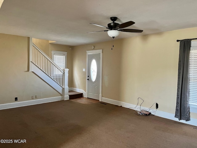 carpeted foyer entrance featuring baseboards, stairs, and ceiling fan