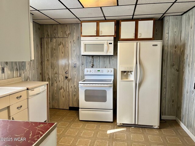 kitchen with white appliances, a drop ceiling, light floors, and wood walls