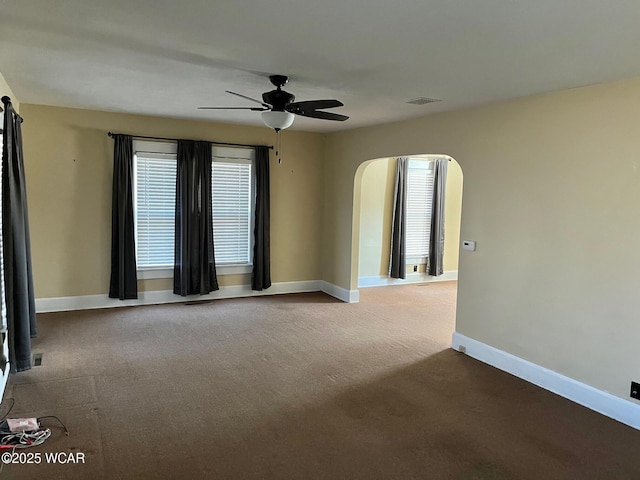 unfurnished room with carpet flooring, baseboards, arched walkways, and ceiling fan