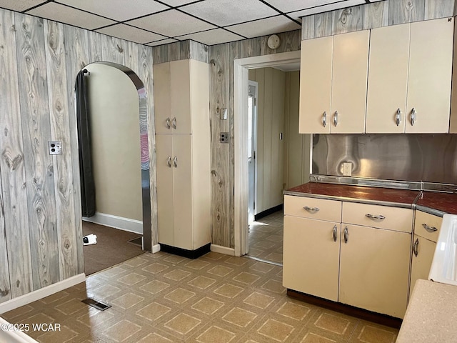 kitchen featuring tile patterned floors, baseboards, a paneled ceiling, and wood walls