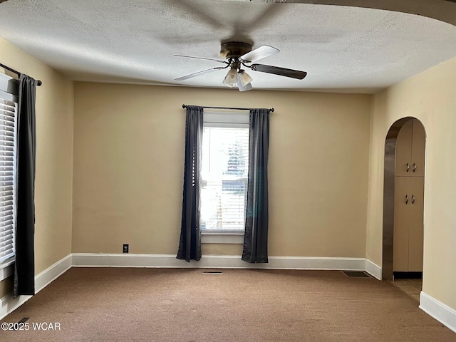 spare room featuring baseboards, ceiling fan, carpet flooring, arched walkways, and a textured ceiling