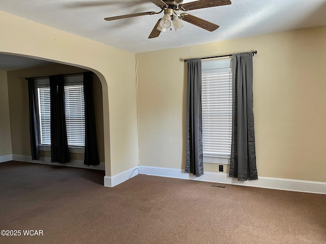 carpeted empty room with arched walkways, baseboards, a textured ceiling, and ceiling fan