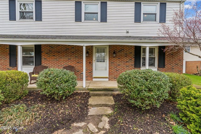 view of exterior entry with a porch and brick siding