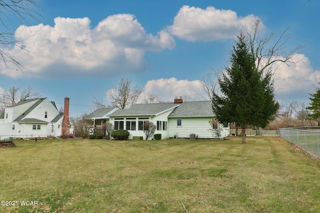 view of front facade featuring a sunroom, a fenced backyard, a chimney, roof with shingles, and a front lawn